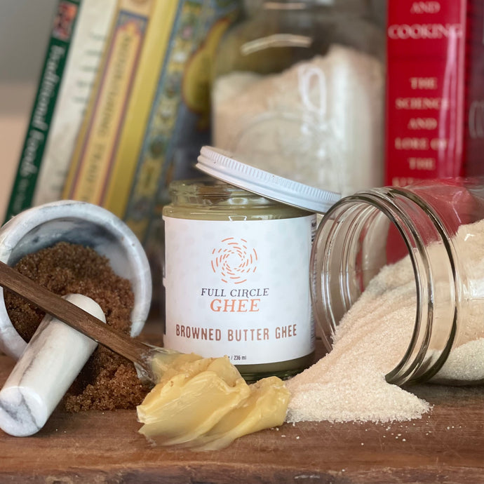 Browned Butter Ghee from Full Circle Ghee arranged with baking cookbooks, flour and sugar on cutting board.
