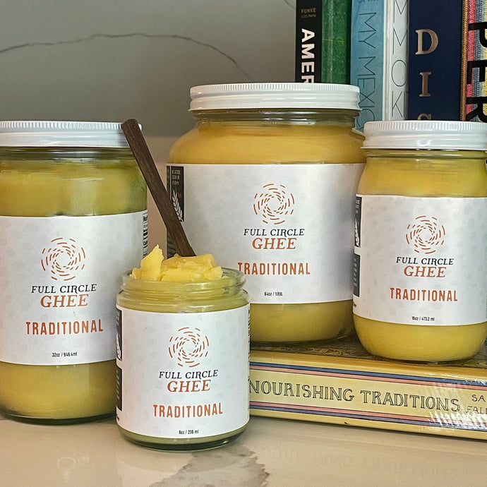 Jars of ghee in various sizes arranged in front of cookbooks.